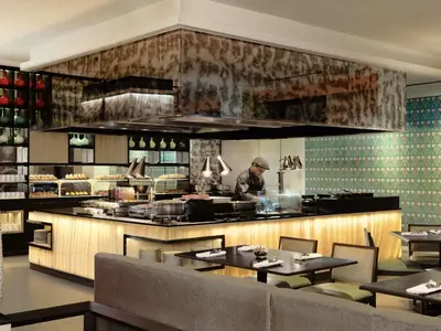 a chef preparing food in a restaurant kitchen with tables at Grand Mercure Bangkok Atrium in Bangkok