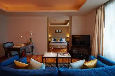 a living room with a blue couch and a bedroom at The Duchess Hotel in Bangkok