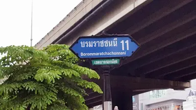 a blue street sign in front of a bridge at Baan Pinklao in Bangkok