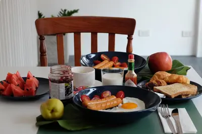 a table with a breakfast of eggs sausage and fruit at Haus Sathorn 21 Bed and Breakfast in Bangkok