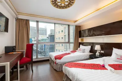 a hotel room with two beds and a desk and a window at Khurana Inn in Bangkok