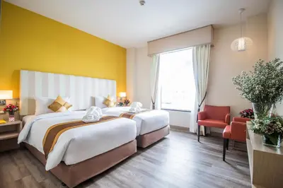 two beds in a hotel room with a yellow wall at Bangkok Midtown Hotel in Bangkok