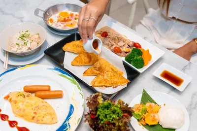 a table topped with plates of food and a person pouring food at Amanta Hotel & Residence Ratchada in Bangkok