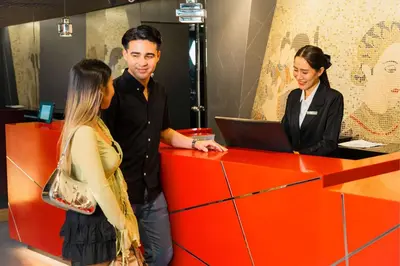 a group of people standing around a red counter with a laptop at Park Plaza Bangkok Soi 18 in Bangkok
