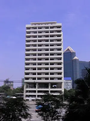 a tall white building with trees in front of a city at Poonchock Mansion in Bangkok