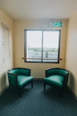 two green chairs in a waiting room with a window at Nonthaburi Palace Hotel in Nonthaburi