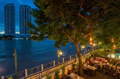 people sitting at a restaurant next to the water at night at New Siam Riverside in Bangkok