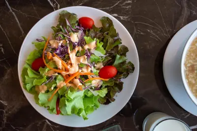 a salad in a white bowl on a table at twothree a homely hotel - SHA Extra Plus in Bangkok