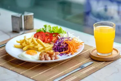 a plate of food with eggs and fries and a glass of orange juice at De Lavender Bangkok Hotel in Bangkok