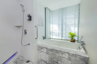 a bathroom with a tub and a shower with a window at LiT BANGKOK Hotel in Bangkok