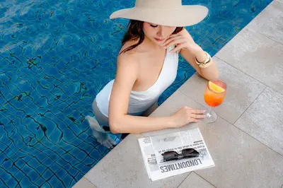 a woman sitting next to a swimming pool with a cocktail and a newspaper at The Westin Grande Sukhumvit, Bangkok in Bangkok
