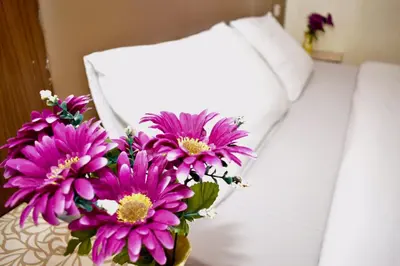 a vase of purple flowers sitting next to a bed at Royal Express Inn in Bangkok
