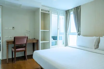 a bedroom with a bed and a desk and a window at Sabai Sathorn Service Apartment in Bangkok