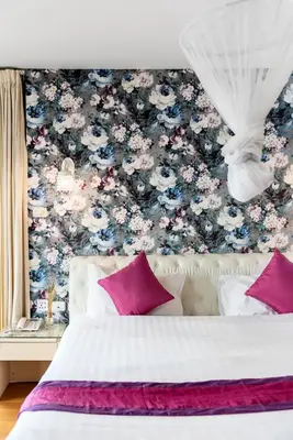 a bedroom with a floral wallpaper with a bed with pink pillows at Nara Suite Residence Bangkok in Bangkok