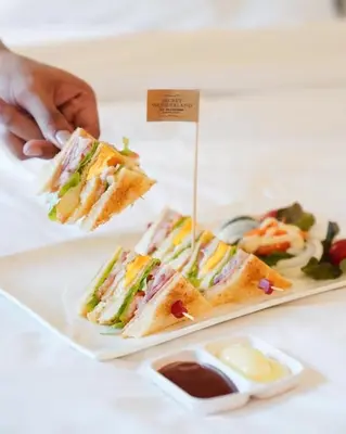 a person holding a plate of sandwiches on a table at Bangkok Oasis Hotel in Bangkok