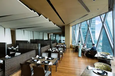 a dining room with tables and chairs and windows at The Okura Prestige Bangkok in Bangkok