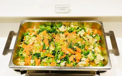 a pan of food with broccoli and carrots at FuramaXclusive Pratunam Park Hotel in Bangkok