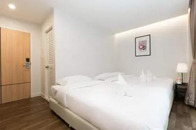 a white bedroom with a large white bed and a door at Metro hotel in Bangkok