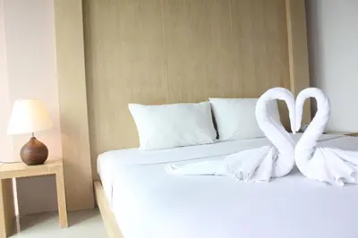 a white bed with two swan towels on it at Bansabai Sabaidee Service Apartment in Bangkok
