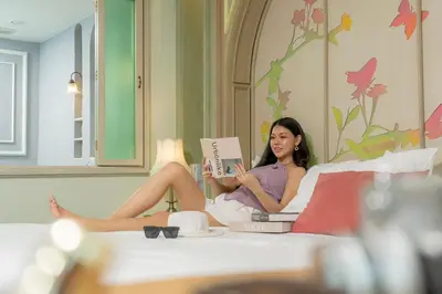 a woman sitting on a bed reading a book at La Petite Salil Sukhumvit 11 in Bangkok
