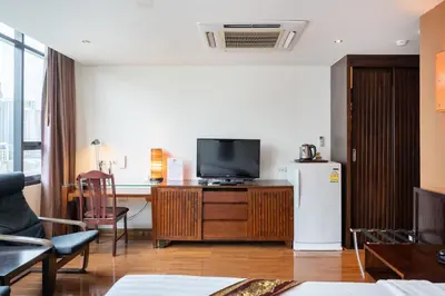 a living room with a tv and a desk and a refrigerator at Hotel Mermaid Bangkok in Bangkok