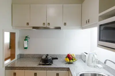 a kitchen with white cabinets and a bowl of fruit on the counter at AT EASE saladaeng by AETAS in Bangkok
