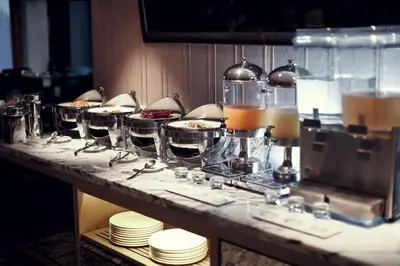 a buffet line with dishes and wine glasses on a table at Arcadia Suites Ploenchit Bangkok in Bangkok