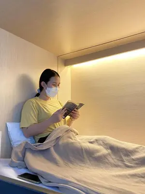 a woman in a bed wearing a mask while reading a book at Cubic Bed Pratunam in Bangkok