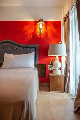 a bedroom with a red wall with a bed and a lamp at Infinite Hotel in Bangkok