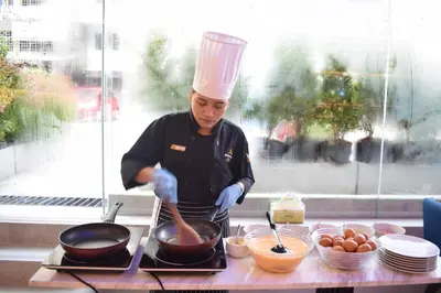 a chef cooking food in a pan on a counter at Aspira One Sutthisan in Bangkok