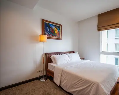 a bedroom with a bed and a lamp and a window at Prime 11, High Floor Over Pool, 2 Br, 2 Balcony in Bangkok