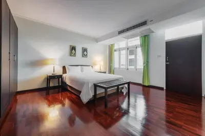 a bedroom with a white bed and a wooden floor at Capital Mansion - SHA Certified in Bangkok