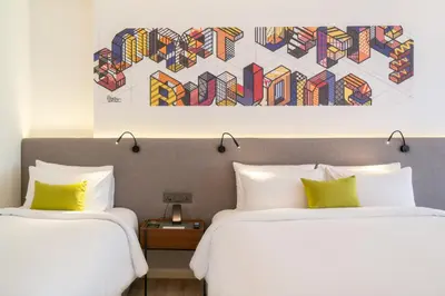 two beds in a hotel room with a painting on the wall at Triple Y Hotel in Bangkok