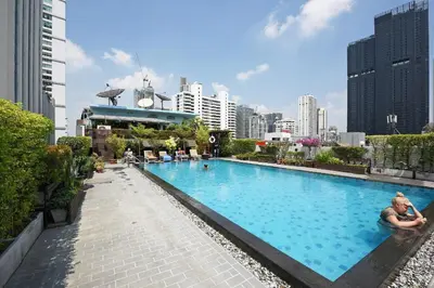 a woman sitting next to a large swimming pool in a city at Ruamchitt Plaza Hotel in Bangkok