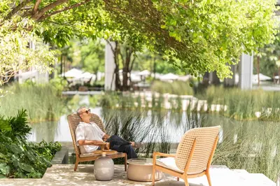 a man sitting in a chair next to two chairs at Four Seasons Hotel Bangkok at Chao Phraya River in Bangkok