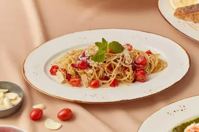 a plate of pasta with tomatoes and basil on a table at Sindhorn Midtown Hotel Bangkok, Vignette Collection by IHG in Bangkok