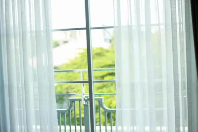 a window with white curtains and a chair looking out at The Square 101 in Bangkok