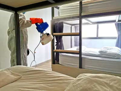 a person in a room disinfecting a bunk bed at Baan Kun Mhor Hostel บ้านคุณหมอโฮสเทล in Bangkok
