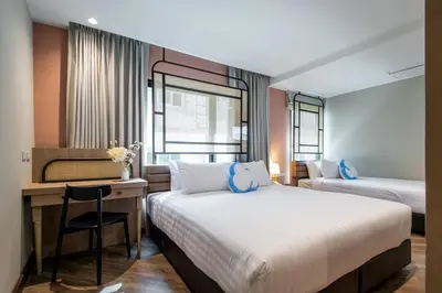 a hotel room with two beds and a desk with a chair at The Cotton Saladaeng Hotel in Bangkok