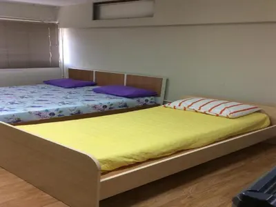 two beds in a bedroom with yellow sheets and purple pillows at Comfortable studio T8 Impact Bangkok Thailand in Nonthaburi