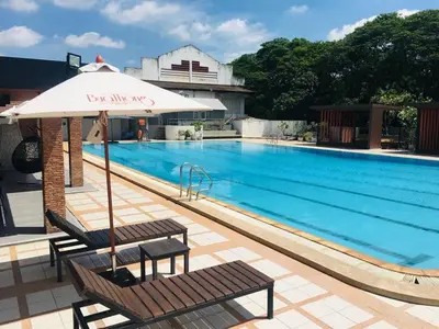 a swimming pool with two benches and an umbrella at Buathong Pool Villa in Ban Khung Taphao