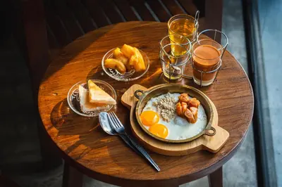 a wooden table with a bowl of breakfast food and glasses of beer at VIX Bangkok at Victory Monument in Bangkok