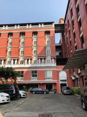 a red building with cars parked in a parking lot at Suda Palace in Bangkok