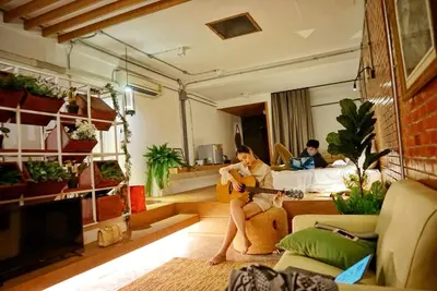 a woman sitting on a couch playing a guitar in a living room at Hidden Habitat - Design Guesthouse in Bangkok