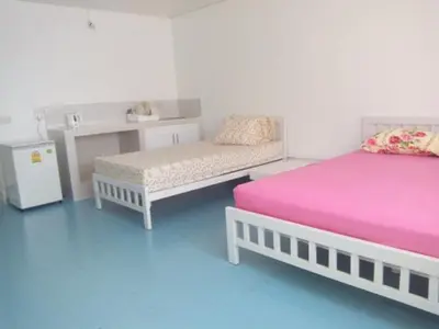 a room with two beds and a bench and a table at Impact Don Mueang Bangkok Guest House in Thung Si Kan