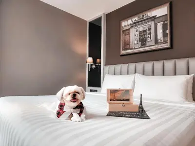 a dog wearing a bow tie sitting on a bed at The Quartier Hotel Phromphong - Thonglor in Bangkok
