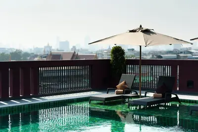 a swimming pool with two chairs and an umbrella at Casa Nithra Bangkok in Bangkok