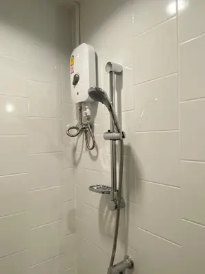 a shower in a bathroom with a white tiled wall at Grasshopper Bed and Cafe in Pak Kret