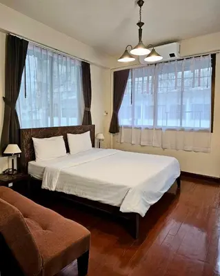 a bedroom with a large bed with white sheets and windows at Baan Glang Soi Restaurant & Guesthouse in Bangkok