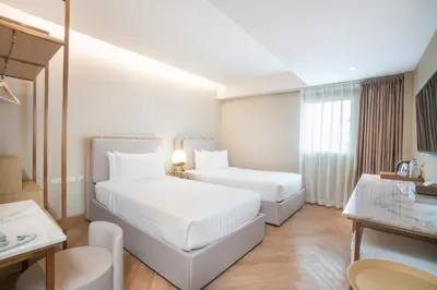 a white room with two beds and a table at Away Bangkok Riverside Kene in Bangkok